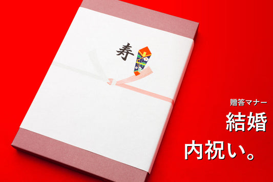 赤い背景に置かれた、寿ののし紙を掛けた結婚内祝いの贈り物
